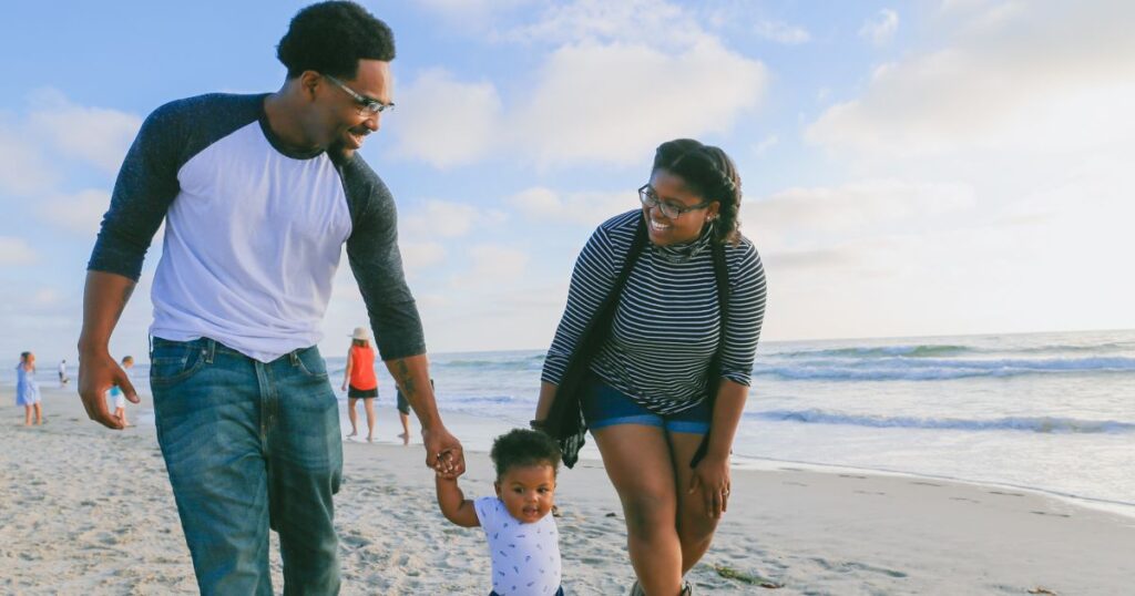 Expat parents walk on a beach, each holding the hand of their child